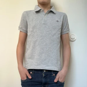 Gant pikétröja - Säljer en snygg grå pikétröja från Gant med klassisk krage och korta ärmar. Tröjan har en broderad logotyp på bröstet. Modellen på bilden är 163cm