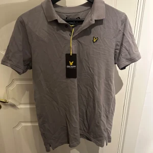 Grå pikétröja från Lyle & Scott - Snygg grå pikétröja från Lyle & Scott. Helt oanvänd med lappen kvar. Storlek 164-170 passar XS