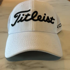 Vit keps från Titleist - Snygg vit keps från titleist med broderad logga i svart framtill. Kepsen har en klassisk design med böjd skärm och justerbar passform. Perfekt för golfentusiaster! Kepsen är i bra skick och ändast använd i 1 vecka, storlek S/M, kan skicka bättre bilder om så önskas. Kom med förslag om pris ifall de inte passar, nytt pris 399kr