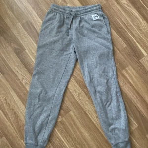 Grå mjukisbyxor från Frank Dandy - Säljer ett par grå mjukisbyxor från Frank Dandy. Byxorna har en elastisk midja med snörning och muddar vid bensluten för en bekväm passform. Perfekta för en avslappnad stil.