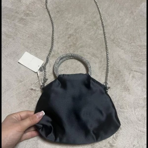 Svart kuvertväska med glittriga detaljer - Svart kuvertväska i satin. 