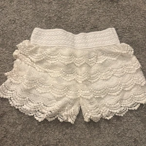 Vita spets shorts - Säljer ett par vita shorts med vacker spetsdesign. De har en elastisk midja och flera lager av spets som ger en fin volangeffekt. Perfekta för en somrig look! 