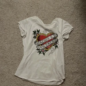 Vit t-shirt med hjärtmotiv från Zadig & Voltaire - Snygg vit t-shirt från Zadig & Voltaire med ett stort hjärtmotiv och blommor på framsidan. T-shirten har korta ärmar och en rund halsringning. Perfekt för en avslappnad stil med en touch av rock'n'roll.