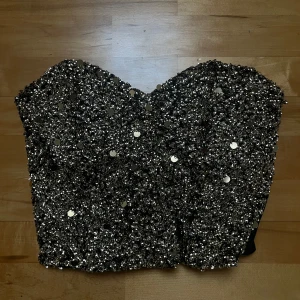 Glittrig svart korsettopp - Säljer en glittrig svart korsettopp med paljetter. Använd cirka några timmar, säljer på grund av inget tillfälle att ha den💕