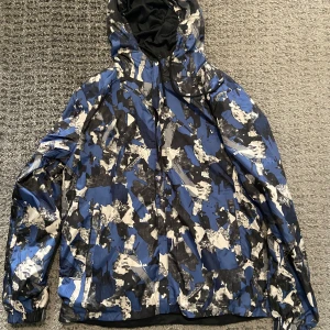 Blå, vit och svart camouflage vindjacka - Säljer en cool vindjacka med blått och svart camouflagemönster. 