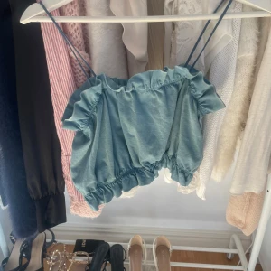 Blå croppad topp från Zara - Säljer en söt blå croppad topp från Zara med smala axelband och elastisk kant. Perfekt för varma sommardagar eller en avslappnad dag på stan.