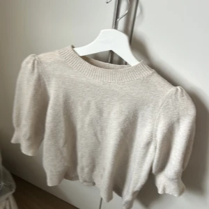 Beige tröja från Vero Moda - Säljer en stilren beige tröja från Vero Moda. Tröjan har en ribbad rund halsringning och puffiga ärmar som ger en trendig look. Perfekt för en avslappnad stil.
