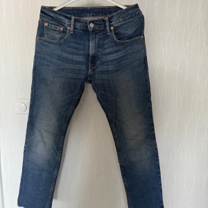 Blå jeans från Levis - Säljer ett par klassiska blå jeans från Levis med en snygg tvätt och femficksdesign. De har en knappgylf och är perfekta för en avslappnad stil. Passar bra till både sneakers och kängor. Byxorna är uppsydda för att passa mig. Jag har storlek 30-32.  Har bara använt jeansen ett fåtal gånger. Har alldeles för mycket jeans, så några behöver säljas. Om du köper jeansen och de inte passar har du returrätt. Du ska vara nöjd om du handlar av mig. 🙂