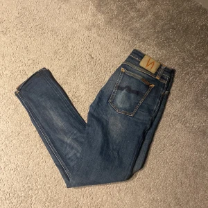 Blå jeans från Nudie Jeans - Snygga blå jeans från Nudie Jeans med klassisk femficksdesign och orange sömmar. Jeansen har en smal passform och är perfekta för en avslappnad stil. Märkeslogga på bakfickan ger en extra touch.