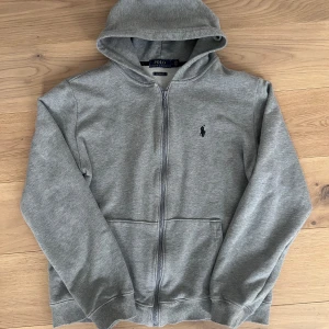 Grå hoodie från Polo Ralph Lauren - Säljer en stilren grå hoodie från Polo Ralph Lauren med dragkedja och klassisk logga på bröstet. Perfekt för en avslappnad look. Den har en bekväm passform och är tillverkad i mjukt material. Hör av dig vid intresse!