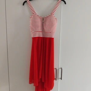 Röd och vit randig klänning - Snygg klänning med randigt mönster upptill i rött och vitt. Den har en dragkedja framtill och axelband. Kjolen är röd och flödig, vilket ger en fin kontrast till den randiga toppen. Passar både S och M.