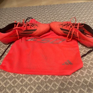  Adidas f50 fotbollskor  - Snygga röda fotbollsskor från Adidas med svarta detaljer och snörning. Skorna har dobbar för bra grepp på planen och kommer med en matchande röd förvaringspåse. Köptes från unisport. Skicket är bra även fast dom e rätt så använda! 