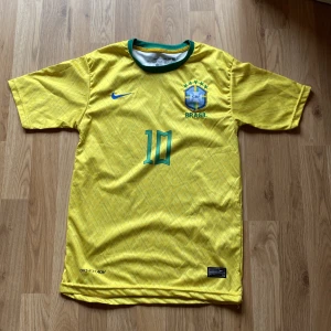 Gul Brasilien fotbollströja Neymar jr 10 - Säljer en gul Brasilien fotbollströja från Nike med nummer 10 och Neymar Jr på ryggen. Tröjan har korta ärmar och ett subtilt mönster. Perfekt för fotbollsfans! 💛💚
