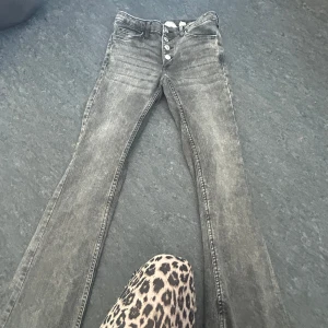 Grå bootcut jeans från H&M - Snygga grå bootcut jeans från H&M med låg midja och justerbar midja. De har en knappgylf med fyra knappar och klassiska femficksdetaljer. Perfekta för en avslappnad stil.