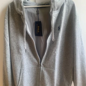Polo Ralph Lauren Zip Hoodie - Säljer en stilren grå zip hoodie från Polo Ralph Lauren. I XL men passar egentligen L, Skick 10/10 helt ny!