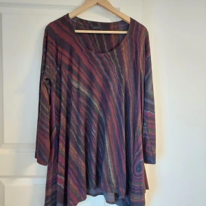 Mönstrad långärmad tröja från Masai - Säljer en färgglad långärmad tröja från Masai med vågiga ränder i lila, rött, grönt och blått. Tröjan har en lös passform och rund halsringning. Perfekt för dig som gillar unika mönster och bekväma plagg.