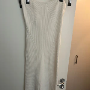 Vit ribbad klänning från Gina - Vit ribbad klänning från Gina Tricot med snygg struktur och diskreta mönster i tyget. Klänningen har en kroppsnära passform och är ärmlös.