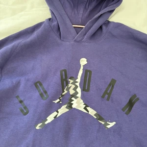 Lila Jordan hoodie  - Säljer en lila hoodie från Jordan med det klassiska Jumpman-loggan i grått och vitt på bröstet. Tröjan ss  har huva och en stor magficka framtill. Perfekt för dig som gillar stilig streetwear.