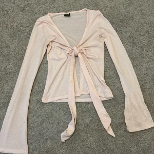 Ljusrosa knytblus från Gina Tricot - Supersöt ljusrosa långärmad blus från Gina Tricot med knyt framtill och v-ringad hals. Tunn och lätt i materialet, perfekt för lager-på-lager eller som den är. Ärmarna är långa och något utsvängda. Säljer då de ej kommer till användning. Använd endast ett par gånger, så den är i väldigt bra skick. Perfekt för sommaren eller våren!💗