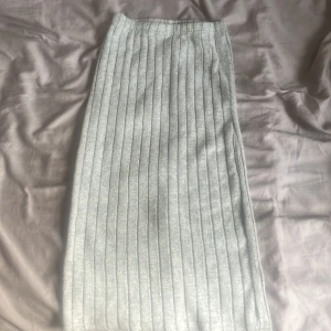 Ljusgrå ribbad långkjol - Säljer en ljusgrå långkjol med ribbad struktur. Kjolen har en rak passform och är stickad, vilket gör den både mjuk och bekväm. Perfekt att styla med en enkel topp eller stickad tröja.