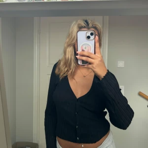 Svart ribbad kofta med v-ringning - Säljer en svart ribbad kofta med v-ringning och knappar framtill. Tröjan är croppad och har långa ärmar. Perfekt att styla med både jeans och kjol. Från Vero Moda i storlek S💕
