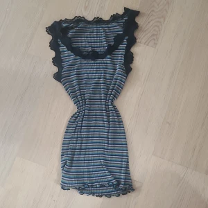 Randig ribbad linne med spetsdetaljer - Finns inget märke! Randig i färgerna svart, blå, lila och grön med spetsdetaljer runt halsen och i botten. 