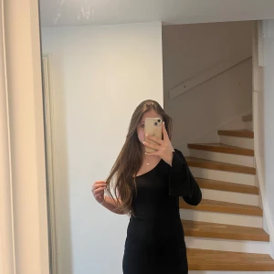 Svart one shoulder ribbad klänning - Säljer en svart, ribbad klänning med one shoulder-design och lång ärm. Klänningen har en tight passform och är tillverkad i ett stretchigt material som sitter snyggt på kroppen. Perfekt för dig som gillar stilrena och trendiga plagg.