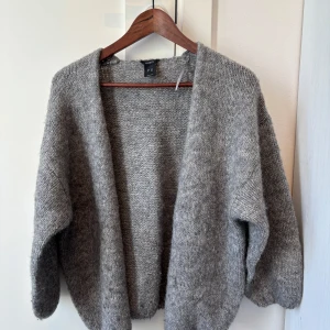 Grå stickad kofta från Lindex - Mysig grå stickad kofta från Lindex med öppen front och lång ärm. Perfekt att slänga på sig över en t-shirt eller blus för extra värme. Enkel och stilren design som passar till det mesta.