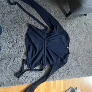 Mörkblå omlottopp med knytband - Säljer en mörkblå omlottopp med långa ärmar och knytband i midjan. Toppen har en v-ringad design och är tillverkad i ett mjukt, lätt material. Perfekt för en stilren och enkel look.