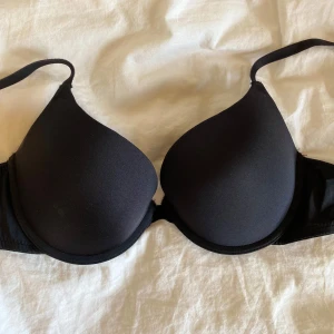 Svart vadderad bh - Svart vadderad bh med släta kupor och justerbara axelband. Klassisk och enkel design som passar till det mesta. Stängs med hyskor bak.
