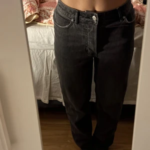 Svarta raka jeans - Säljer ett par svarta jeans med raka ben och klassisk femficksdesign. Jeansen har normal passform och silverfärgade knappar och nitar. Perfekta till vardags och enkla att matcha med olika toppar.