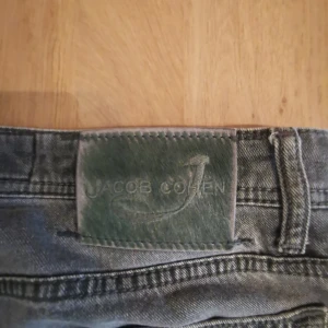 Grå jeans från Jacob Cohen - Säljer ett par grå jeans från Jacob Cohen med klassisk femficksdesign och raka ben. Jeansen har en snygg tvätt och patch med logga bak i midjan. Perfekta för dig som gillar stilrena och tidlösa jeans.