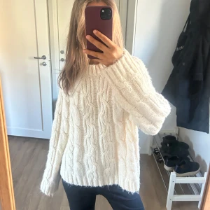 Vit stickad kabelstickad tröja - Mysig vit stickad tröja med kabelstickat mönster och lång ärm. Tröjan har en avslappnad passform och rund halsringning. 