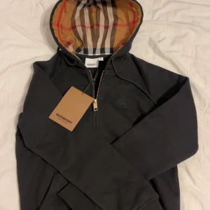 Svart hoodie från Burberry med klassisk rutig huva - Säljer en svart hoodie från Burberry med dragkedja och den ikoniska rutiga huvan i beige