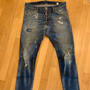 Blå  jeans från Dsquared2 med slitningar - Säljer ett par blå jeans från Dsquared2 med slitningar. Jeansen har klassisk femficksdesign, knappgylf och tydliga slitdetaljer både fram och bak. Snygg tvätt och coola detaljer för en trendig look. Fler bilder via dm!
