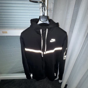 Svart zip-hoodie från Nike med reflexdetaljer - Svart hoodie från Nike med dragkedja. Storlek M.