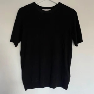 Svart stickad tröja från Amisu - En enkel svart stickad tröja från Amisu. Tröjan har korta ärmar och rund halsringning, perfekt för en stilren och clean look. Passar till många olika outfits och är lätt att matcha.