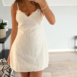 Vit klänning - Söt vit kortklänning med smala axelband och v-ringad byst. Klänningen har fina spetsdetaljer och en lätt figurnära passform. Perfekt för sommaren eller student. Använd max 1 gång, helt i nyskick