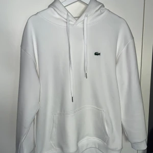 Vit hoodie från Lacoste - Ny köpt använd två gånger pga för kort i armarna för min del. Väldigt snygg stilren och inga defekter. Hör av vid frågor!