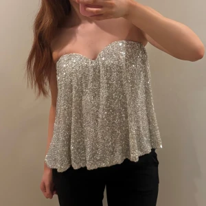 Glittrig silver tubtopp från Gina Tricot - Helt oanvänd, endast provad! Säljer en glittrig silverfärgad tubtopp från Gina Tricot. Toppen är axelbandslös och har en lätt utsvängd passform.