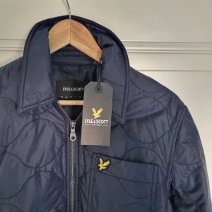 Mörkblå quiltad overshirt från Lyle & Scott - Säljer en mörkblå quiltad overshirt från Lyle & Scott. Jackan är size Small. Orginal priset är 1200kr men jag säljer den för 470kr. Den är helt oandvänd och är i perfekt skick. Jag säljer den pågrund av att den inte passar mig då den är för liten.