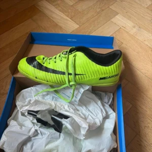 Neongröna fotbollsskor med svart detalj - Säljer ett par neongröna fotbollsskor från MOEDAHONG med svart sidoswoosh och snörning. Skorna har låg profil och är designade för bra grepp på planen. Perfekta för dig som vill sticka ut på fotbollsplanen.