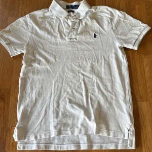 Vit pikétröja från Polo Ralph Lauren - Klassisk vit pikétröja från Polo Ralph Lauren med broderad logga på bröstet. Tröjan har krage, knappar vid halsen och korta ärmar. Perfekt för en stilren och tidlös look.                                                Går att få ner priset lite (typ 50kr max) skit bra skick, har växt ut.