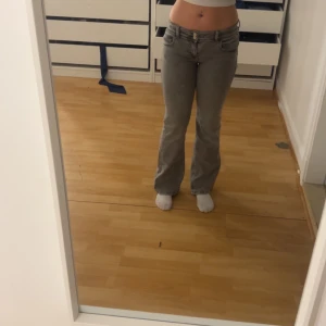 Grå bootcut jeans med stjärndetalj - Säljer ett par gråa bootcut jeans med låg midja och en snygg stjärna på bakfickan. Jeansen har klassisk femficksdesign och dragkedja framtill. Perfekta för dig som gillar en avslappnad men trendig stil. Dessa är från ginas barnavdelning så de e i storlek 164 och passar xs