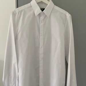 Vit klassisk skjorta från H&M - Säljer en stilren vit skjorta från H&M med klassisk krage, långa ärmar och knäppning framtill. Skjortan har knappt använts och är i toppskick. Storlek: M