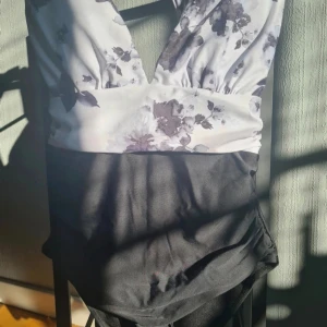 Oanvänd baddräkt i väldigt fin design med knytning - Väldigt fin svart/vit baddräkt med blommig överdel som knyts i nacken.  !ENDAST TESTAD MED UNDERKLÄDER PÅ!  Alla kläder rollas innan de skickas då katt finns i hemmet!🐈  #storleks #baddräkt #bathingclothes #sverige #wilmabooksstorleks