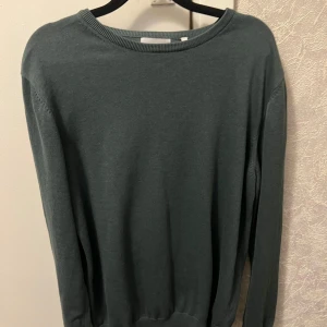 Mörkgrön tröja från Bläck - Säljer en stilren mörkgrön tröja från Bläck i storlek L. Tröjan har rund halsringning och långa ärmar, perfekt för lager-på-lager eller som den är. Enkel och klassisk design som passar till mycket.