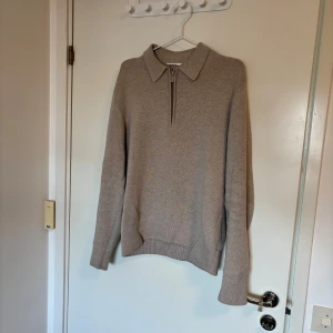 Beige tröja med dragkedja - Säljer en beige tröja med krage och halv dragkedja framtill. Tröjan har lång ärm och ribbade muddar vid ärmslut och nederkant. Perfekt för lager-på-lager och enkel att matcha med olika outfits. Använd få gånger men finns en lite fläck av missfärgat tyg på framsidan, tröjan köptes ny med missfärgningen så inget orsakat av användning.