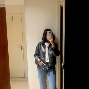 Svart skinnjacka  från Stockholm  - Säljer en svart skinnjacka med klassisk krage och dragkedja framtill. Jackan har en boxig, croppad passform och stora fickor framtill. Inköpt förra våren på MQ (märket stockhom) 1700:- knappt använd.