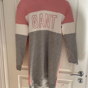 Rosa och grå huvklänning från GANT - Säljer en långärmad huvklänning från GANT i rosa, grått och vitt. Klänningen har stor GANT-logga framtill och texten GIRLS på ryggen.  Sparsamt använd och i fint skick. Storlek barn 170. Möjligt att den har en mindre fläck på framsidan men den är isåfall knappt märkbar 